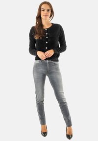 Cardigan nero e peloso con scollatura rotonda e bottoni perla, abbinato a jeans aderenti grigi chiari e décolleté nere a punta.