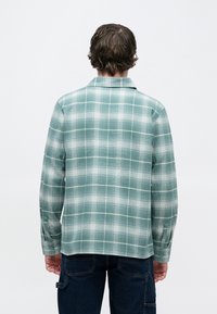 Πράσινο φανελένιο πουκάμισο με καρώ μοτίβο, μακριά μανίκια και γιακά. Διαθέτει απαλή υφή, αντίθετες λευκές γραμμές και ίσια βάση.