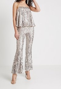 Silvrig paljett-tvådelad outfit med en design av utsvängda byxor. Toppen har tunna band och en lager-effekt som visar en glänsande textur.