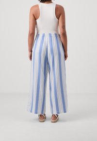 Luftiga byxor med vida ben i ljusblått och vita vertikala ränder, tillverkade av lätt tyg; bärs med en åtsittande vit tanktopp; elastisk midja.