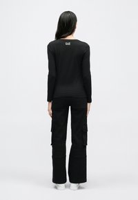 Svart långermet topp med rund hals, med en liten logo på baksiden. Kombinert med svarte cargobukser og hvite joggesko.