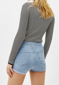 Svart och vit randig långärmad topp i kombination med ljusblå högmidjade denimshorts, som har två bakfickor och uppvikta ärmslut.