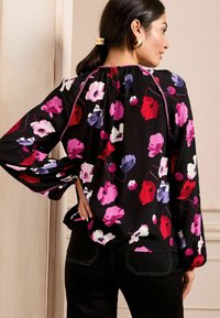 Blusa nera con motivi floreali rosa, rossi e viola. Presenta maniche lunghe, un collo arricciato e una delicata rifinitura.
