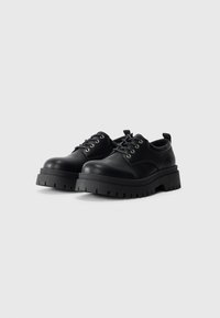 Zapatos de cuero negro con suela de plataforma gruesa, puntera redondeada y cierre de cordones. Presenta ojales metálicos y una lengüeta en la parte posterior.