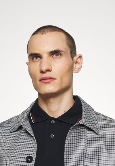 Plaid shirt jacket with gray and black tones, featuring a collared neck, button closure, and a navy blue polo underneath.