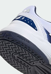 Weißer Sportschuh mit strukturierter navyblauer Sohle, atmungsaktivem Mesh-Obermaterial und einem glänzenden blauen Akzent mit Perforationen zur Belüftung.