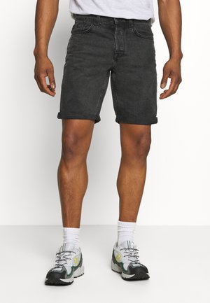 Shorts en denim noir avec ourlets roulés, design à cinq poches et coupe classique. Assortis avec des chaussures de sport grises et vertes et des chaussettes blanches.