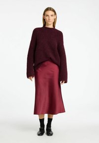 Burgundy fluffig tröja med överdimensionerade ärmar i kombination med en satin burgundy midikjol, svarta strumpor och svarta skor. Slät textur genom hela outfiten.