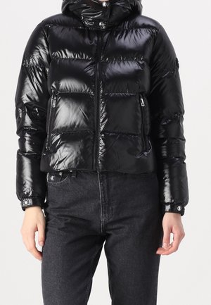 Lyhyttaskuinen musta untuvapusero, jossa on kiiltävä pinta, huppu, vetoketjullinen etuosa ja kaksi etutaskua, joissa on napilliset suljinteet.