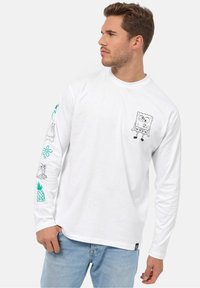 Hvid langærmet t-shirt med en sort kontur af Spongebob-graphic på brystet. Farverige karakterdesigns på ærmerne med blå og grønne accenter.