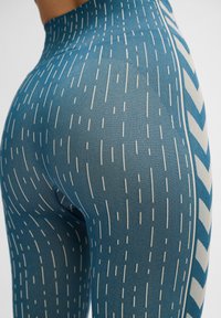 Blå mönstrade leggings med vertikala vita ränder och en chevron-design på sidan, gjorda av ett flexibelt, strukturerat material.