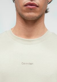 Light gray cotton t-shirt with a crew neck, featuring a subtle embroidered Calvin Klein logo on the chest. Smooth texture, minimalist design.