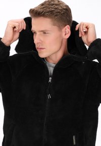 Czarna polarowa kurtka z kapturem, zapinana na zamek, z bocznymi kieszeniami. Miękka w dotyku, o casualowym stylu, idealna na chłodniejszą pogodę.