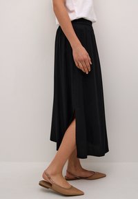 Svart midi kjol med elastisk midja, med en sidoklyvning. Kombinerad med tanfärgade ballerinas, vilket framhäver en minimalistisk design.