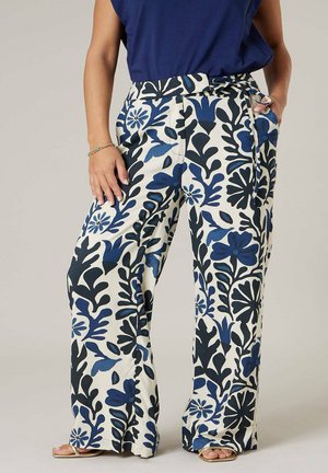 Femme portant un pantalon à jambes larges avec un motif floral bleu et noir, associé à un haut bleu marine et des sandales ouvertes.