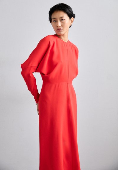 Vestido rojo de manga larga con cuello alto y mangas sueltas y drapeadas. Tejido suave con una silueta recta y una costura en el frente.