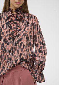 Lyserød leopardprint-bluse med flæsekrave og manchetter, der har en glat tekstur og løs pasform, kombineret med en ensfarvet lyserød nederdel.