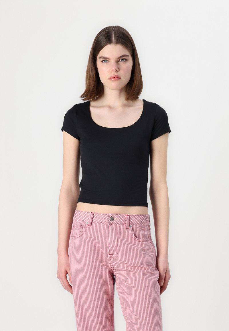 Čierny, tesne priliehajúci crop top s krátkymi rukávmi a okrúhlym výstrihom, skombinovaný s ružovými a bielymi pásikavými nohavicami s vysokým pásom.