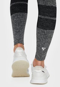 Černé a šedé legíny se vzorem a žebrovanou texturou, spárované s bílými sportovními botami s texturovanou podrážkou a minimálním designem.