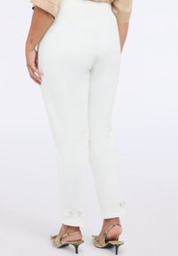 Witte fitted broeken met een gladde textuur en knopen bij de enkels, gecombineerd met gemusterde sandalen met een lage hak.