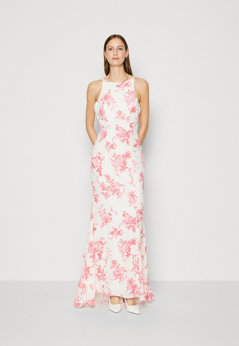 Robe maxi fleurie blanche avec des motifs roses, sans manches et avec une jupe fluide. Portée avec des talons beiges. Texture de tissu lisse.