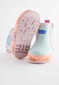 Bottes de pluie en caoutchouc bleu clair avec semelles roses, arborant un logo "Peppa Pig" et un motif de éclaboussures sur le bord inférieur. Semelle extérieure texturée antidérapante.