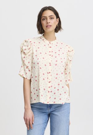 Light yellow blouse with puffed short sleeves, featuring red polka dots, a collar, and button front. Made of a textured, soft fabric.