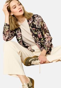 Floral print jacket with black background, ivory top, beige wide-leg pants, and green-brown sneakers with gold accents and textured soles.