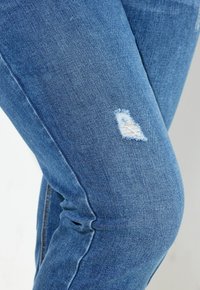 Vaqueros de mezclilla azul claro con un patrón desgastado y agujeros deshilachados cerca de la rodilla, ajuste slim con una textura suave.