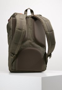 Vista trasera de una mochila de tela verde oliva con correas de hombro acolchadas y panel trasero de malla transpirable sobre una superficie blanca.