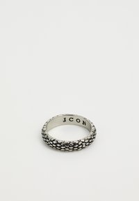 Bague en argent texturé avec un motif en écailles et "J CON" gravé à l'intérieur de l'anneau, placée sur un fond blanc uni.