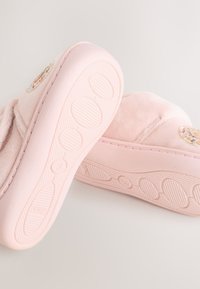Bløde lyserøde babysko med teksturerede såler og broderet cirkeldesign på siderne, vist fra bund- og sidevinkler.