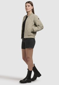 Lichtgrijze gequilt bomberjack met ribbels aan de mouwen, gecombineerd met zwarte denim shorts en zwarte enkelboots. Eenvoudig, modern ontwerp.