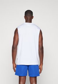 Bílý bezrukávový tričko skombinované s modrými síťovými sportovními šortkami. Tkanina vypadá hladce a střih je uvolněný s kulatým výstřihem.