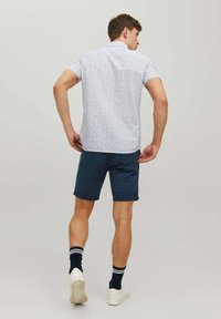 Cămașă cu mânecă scurtă din material ușor, cu un imprimat mic și colorat, combinată cu șorturi bleumarin și adidași albi, oferind un aspect casual.