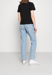 Czarny t-shirt z krótkim rękawem w połączeniu z jasnoniebieskimi dżinsami. Białe trampki typu high-top dopełniają casualowy wygląd.