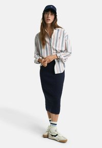 Camicia a maniche lunghe a righe bianca, blu e rossa; gonna blu in maglia a trecce; berretto blu; sneakers bianche con dettagli neri e calze a righe.