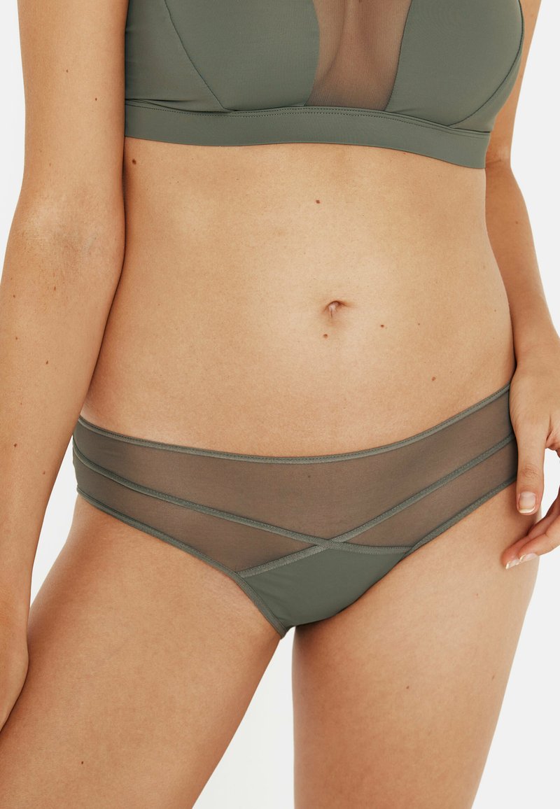 Sous-vêtements olive avec un mélange de tissu lisse et de panneaux en maille transparente, dotés d'un design taille basse et de lignes d'accent qui se croisent.