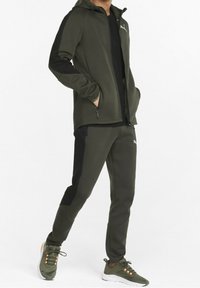 Olijfgroene sportieve trainingsoutfit van zacht materiaal, bestaande uit een capuchonjack met ritszakken en bijpassende broek met zwarte accenten.