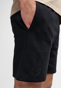 Svarta träningsshorts med en slät textur, utrustade med fickor och ett subtilt chevronmönster präglat på den nedre sidan.
