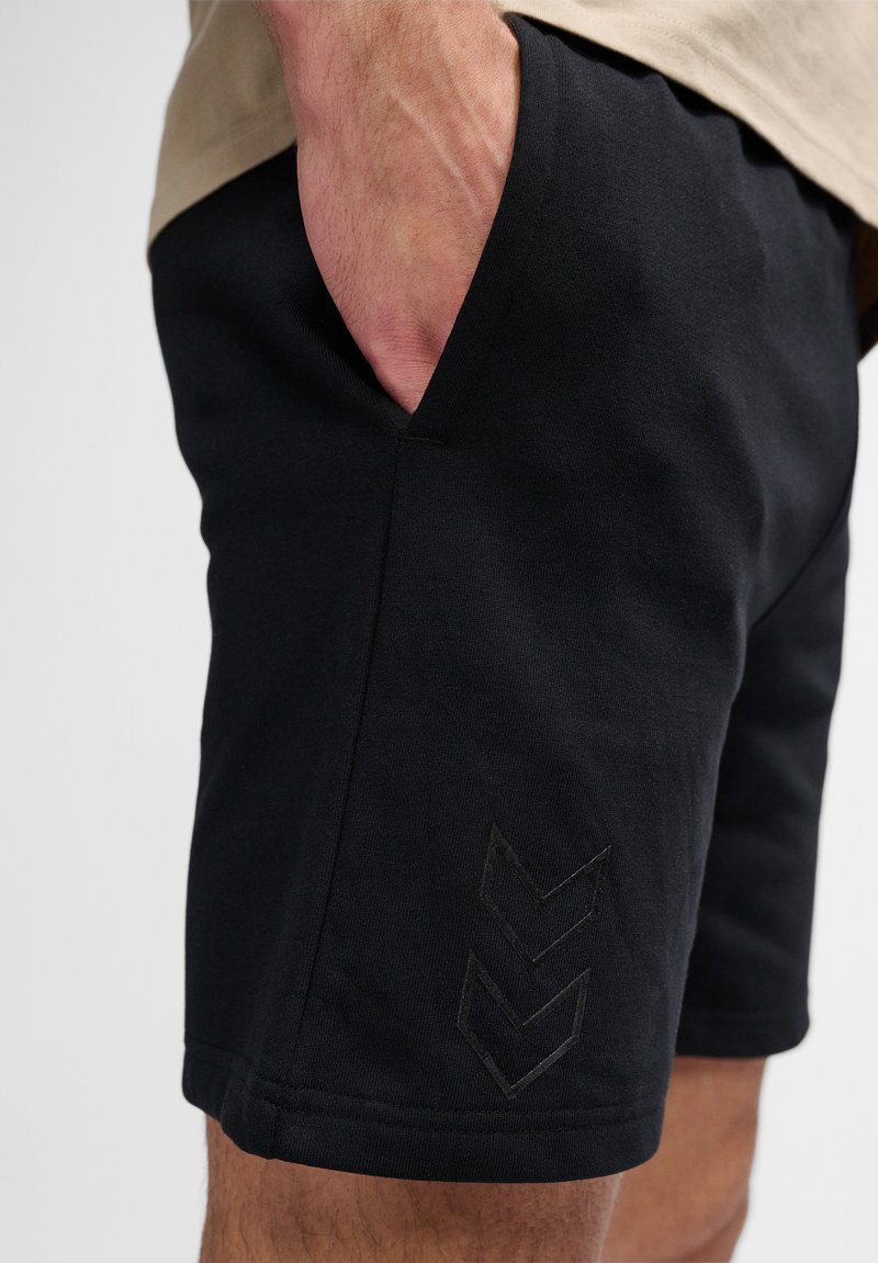 Svarta träningsshorts med en slät textur, utrustade med fickor och ett subtilt chevronmönster präglat på den nedre sidan.