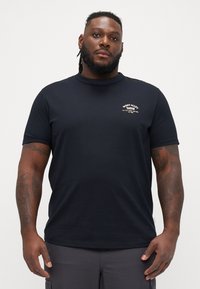 Tricou din bumbac negru, cu guler rotund și mâneci scurte. Prezintă un logo alb pe partea stângă a pieptului. Design mulat și textură moale.