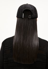 Schwarze Baseballmütze mit verstellbarem Riemen hinten, im Kontrast zu glattem, langem schwarzen Haar. Getragen mit einem strukturierten schwarzen Pullover.