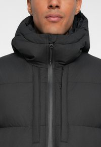 Giacca a vento nera con colletto alto, dotata di zip frontale e due tasche laterali. Texture trapuntata leggera e tessuto liscio.