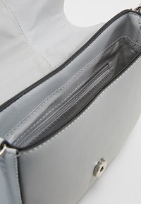 Interiér šedé kožené kabelky s kapsou na zip, hladkou texturou a stříbrným kováním. Zavírání na klopu s zaobleným výřezem.