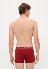 Piros pamut boxer alsónemű fehér derékpánttal, amelyen a "TOMMY HILFIGER" logó látható, hátulról látható egy mezítelen törzsön.