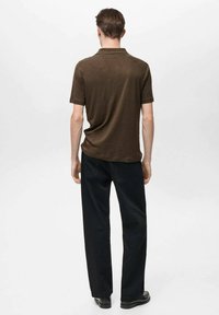 Tmavě hnědá polo košile s krátkým rukávem, kombinovaná s volnými černými džíny a černými botami, pohled zezadu. Jednoduchý design, strukturovaná tkanina.