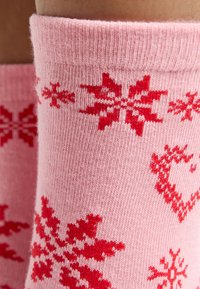 Calcetines de lana de color rosa con patrones de copos de nieve y corazones rojos. La textura es suave con un acabado acanalado uniforme en el puño.