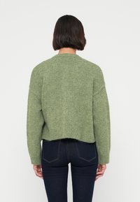 Πράσινο πλεκτό πουλόβερ με χαλαρή εφαρμογή, στρογγυλή λαιμόκοψη και ελαφρώς κοντό τελείωμα. Μαλακή υφή και ραφές ώμων που πέφτουν χαμηλά.