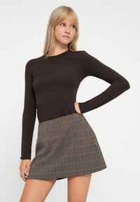 Langermet brun topp med en tettsittende design, kombinert med et kort rutete skjørt i brune og gråtoner, vist i en sidevisning.